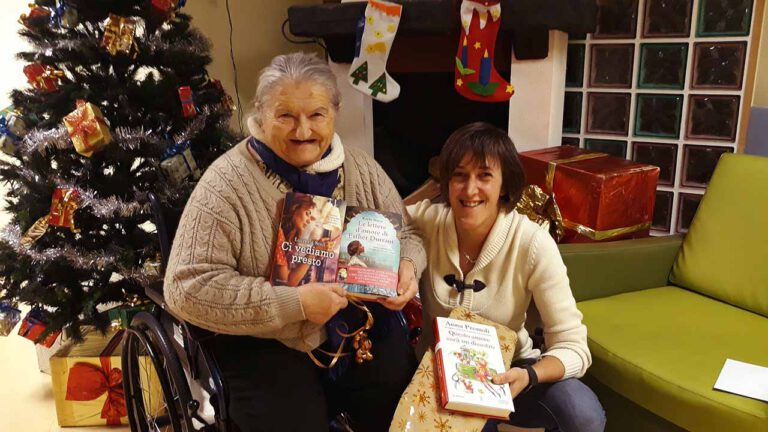 Anziana e "nipote di Babbo Natale" sorridono con libri in mano