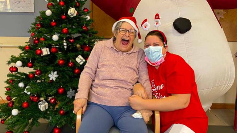 Anziana con cappello di Babbo Natale con operatrice RSA