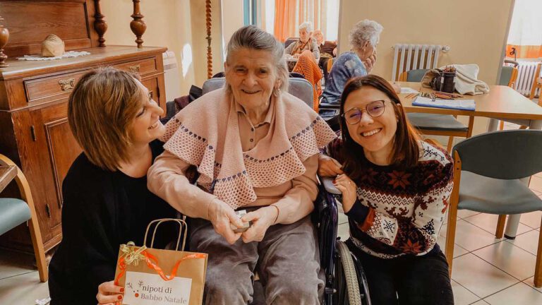 Due "nipoti" con anziana sorridono grazie al progetto Nipoti di Babbo Natale