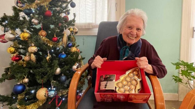 Anziana che sorride con in mano un pacco dono di Nipoti di Babbo Natale